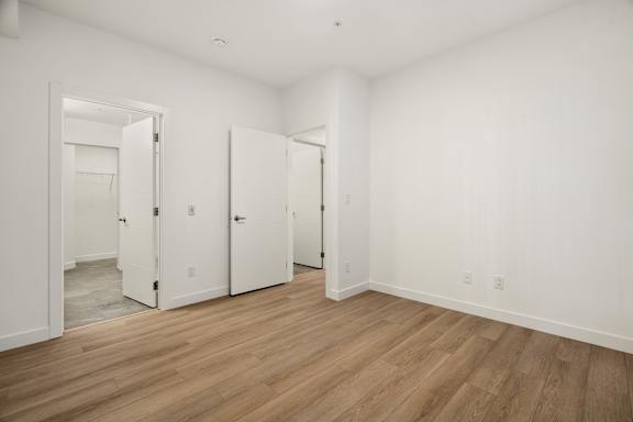 A room with white walls and wooden flooring with three doors.