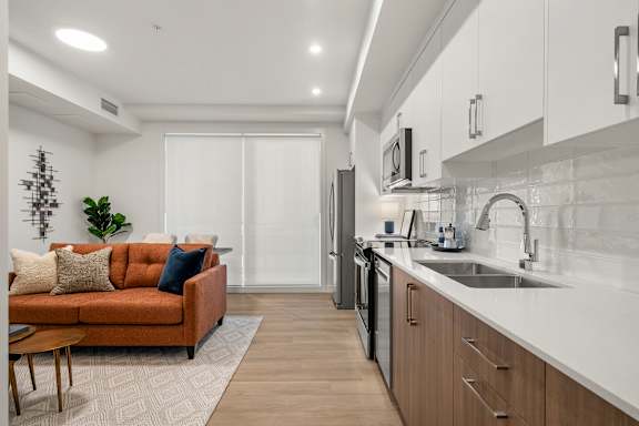 A modern kitchen with a brown sofa and wooden cabinets.
