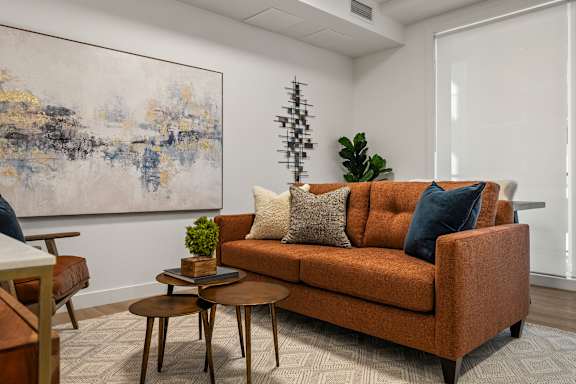 A living room with a brown couch and a blue and white abstract painting on the wall.