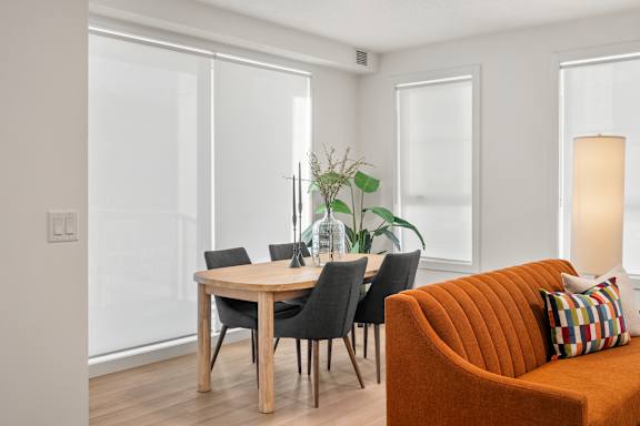 A living room with a brown couch, a table with chairs, and a plant.