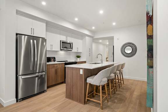 A modern kitchen with a refrigerator, microwave, and bar stools.