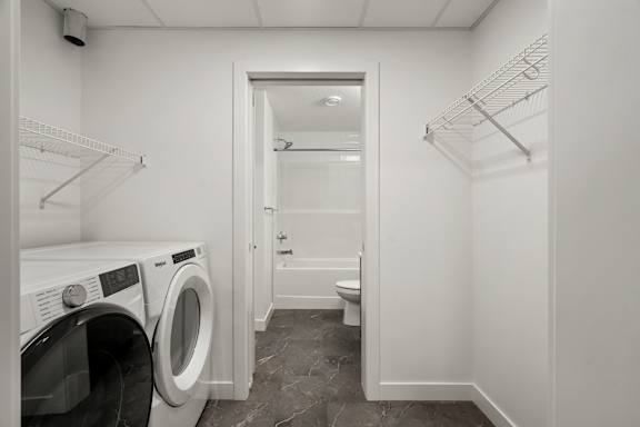 A laundry room with a washer and dryer on the left and a toilet in the doorway.