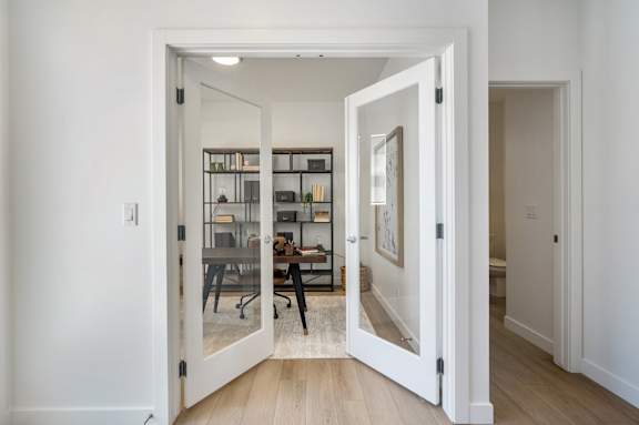 A white doorway opens to a room with a desk and chairs.