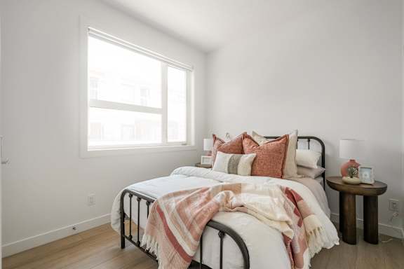 A bedroom with a bed, pillows, a blanket, and a small table.