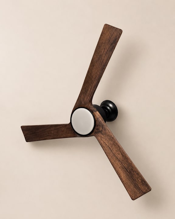 A wooden fan with a black knob is mounted on a wall.