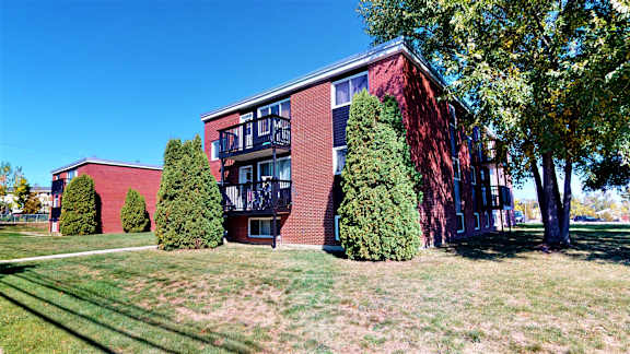 A red brick building with a balcony and trees in front.