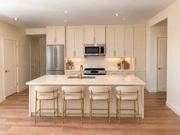 A kitchen with a white countertop and white bar stools.