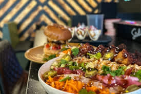A bowl of food with a burger and other food items in the background.