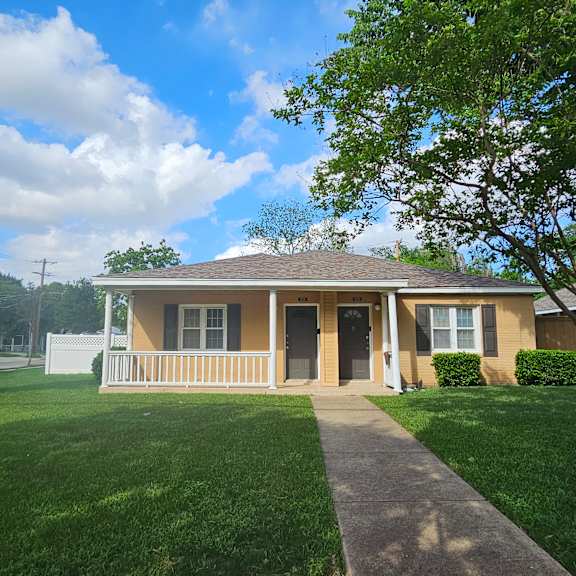 A yellow house with a white fence and a green lawn.
