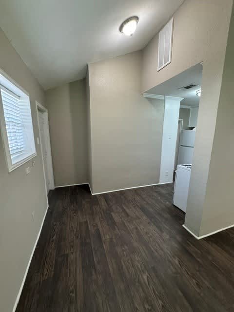 A room with a white fridge and wooden floors.