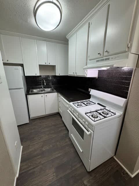 A small kitchen with a white stove and black countertops.