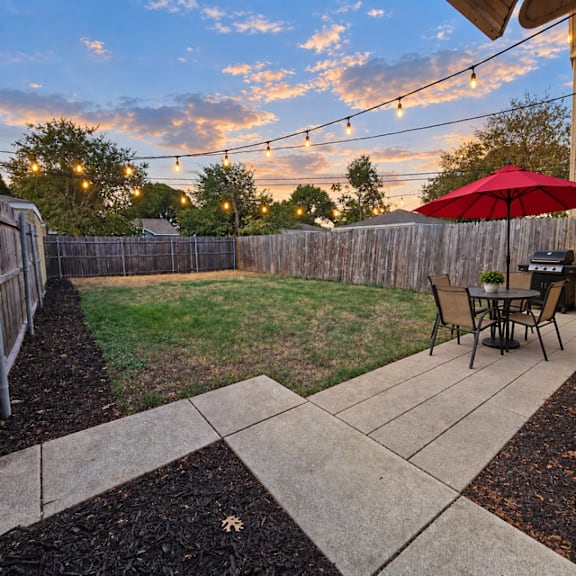 A backyard with a table and chairs under a red umbrella.