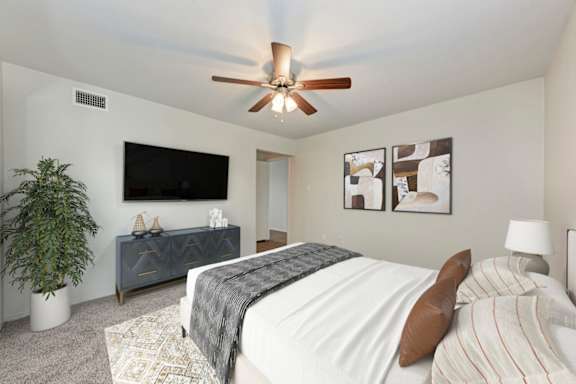 A bedroom with a bed, a ceiling fan, and a plant.