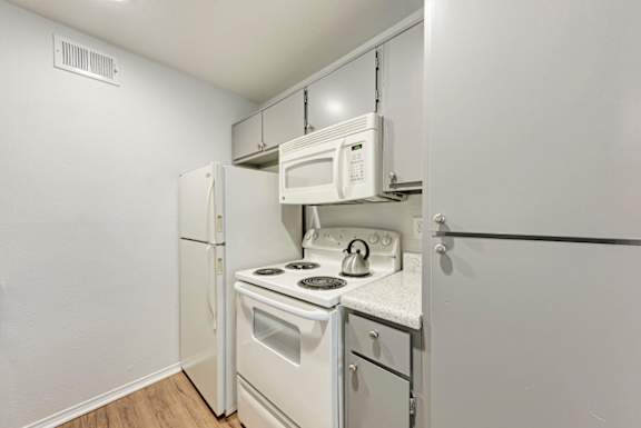 A small kitchen with a white refrigerator, oven, and microwave.