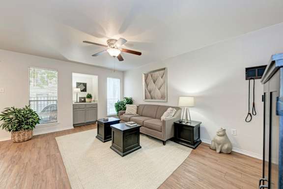 A living room with a couch, a table, a plant, and a fan.