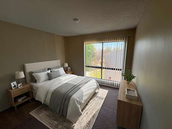 A bedroom with a large bed and a window overlooking a fence.