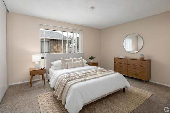 A bedroom with a large bed, a nightstand, and a window with blinds.