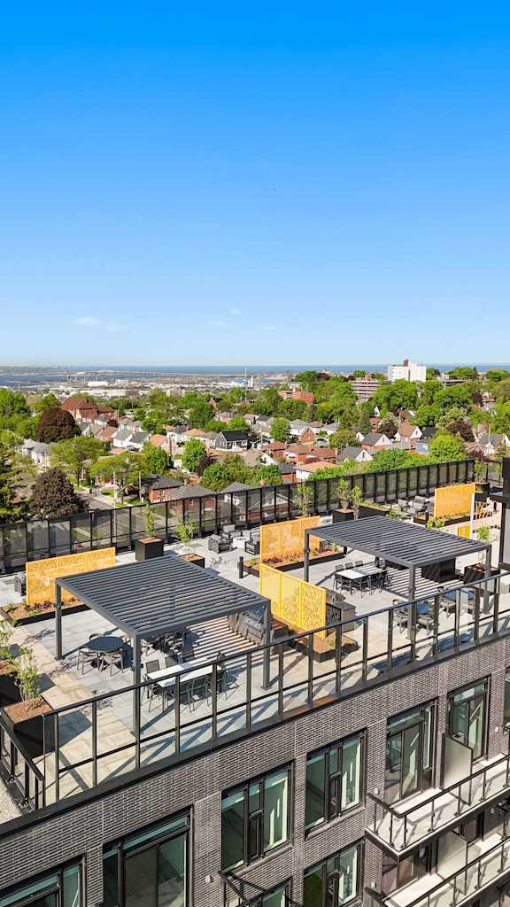 A rooftop patio with a table and chairs overlooks a cityscape.