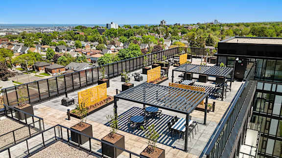 A rooftop patio with tables and chairs overlooks a cityscape.