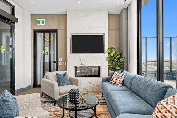 A modern living room with a grey sofa, a fireplace, and a flat-screen TV mounted on the wall.