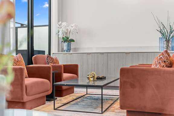 A living room with a glass table and orange chairs.