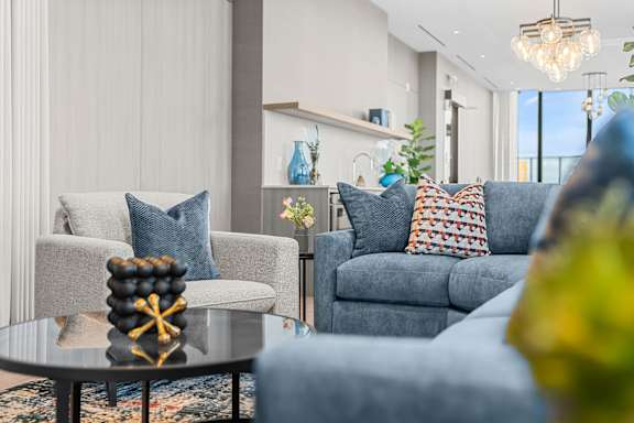 A living room with a grey couch, a grey armchair, a coffee table with a decorative item on it, and a plant in the corner.