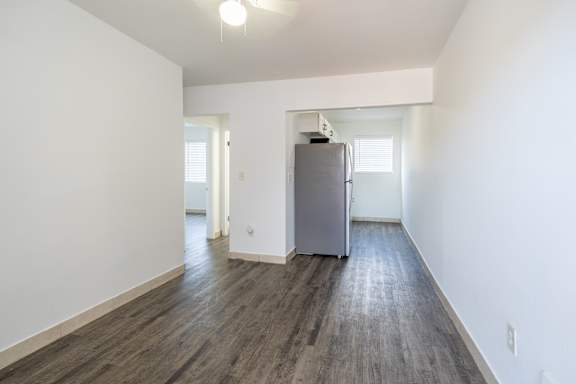 A room with a grey fridge and wooden floors.