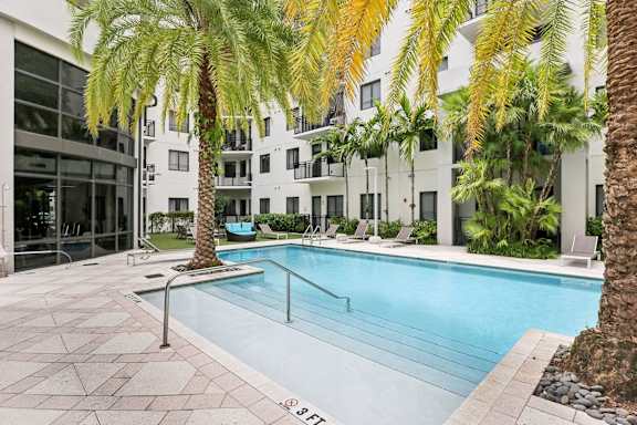 A pool surrounded by palm trees and a building in the background.