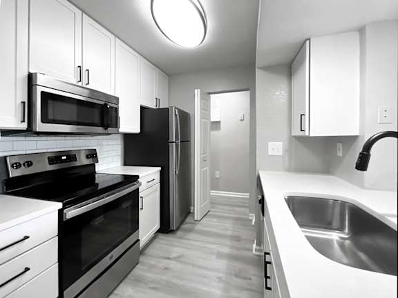 A black and white image of a kitchen with white cabinets, black appliances, and a white counter.