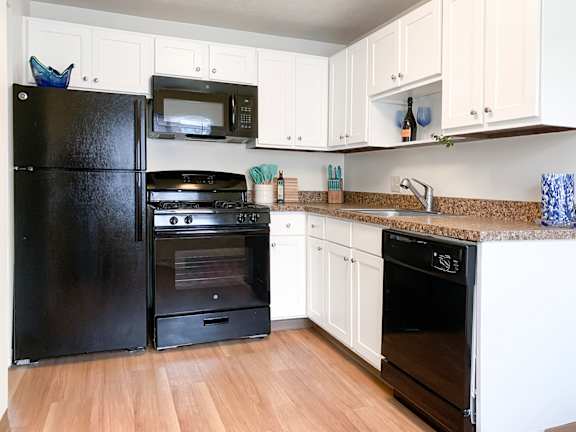 A black refrigerator and oven in a kitchen with white cabinets.