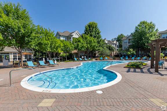 A swimming pool surrounded by trees and lounge chairs.