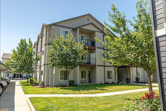 Apartment building with green lawn and trees in front.