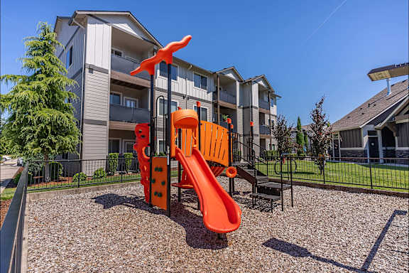 A playground with a slide and a climbing frame in front of a residential building.