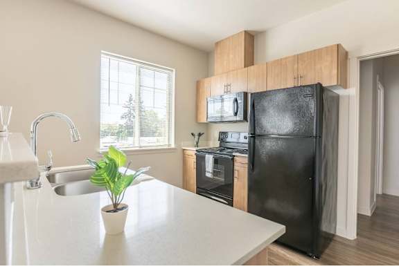 A black refrigerator is in a kitchen with a sink and a window.