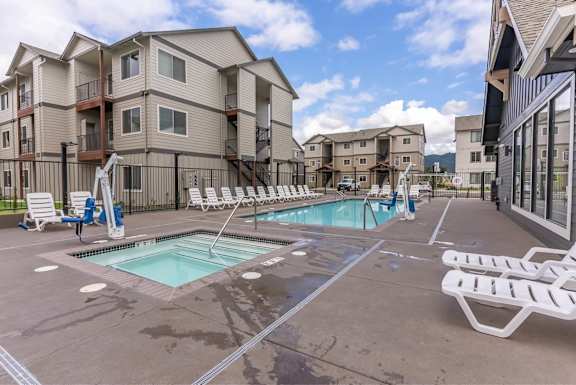 A swimming pool surrounded by lounge chairs in front of apartment buildings.