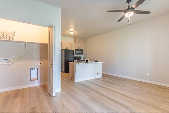 A room with a ceiling fan and a kitchen area with a microwave and oven.