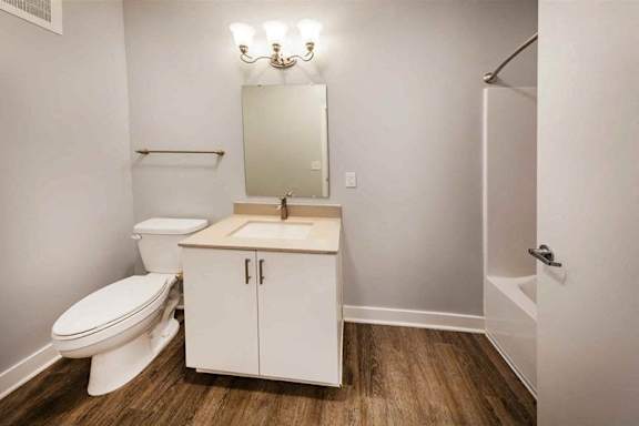 A white bathroom with a toilet, sink, and wooden floors.