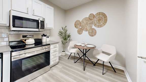 A kitchen with a stove, oven, microwave, and a dining table with chairs.
