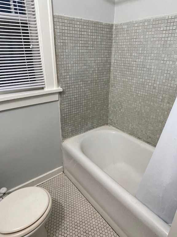 A white toilet sits next to a bathtub in a bathroom with grey tiles.