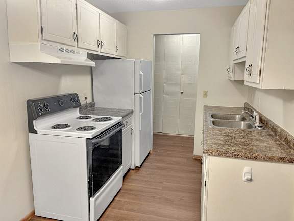 A kitchen with a white stove, refrigerator, and cabinets.