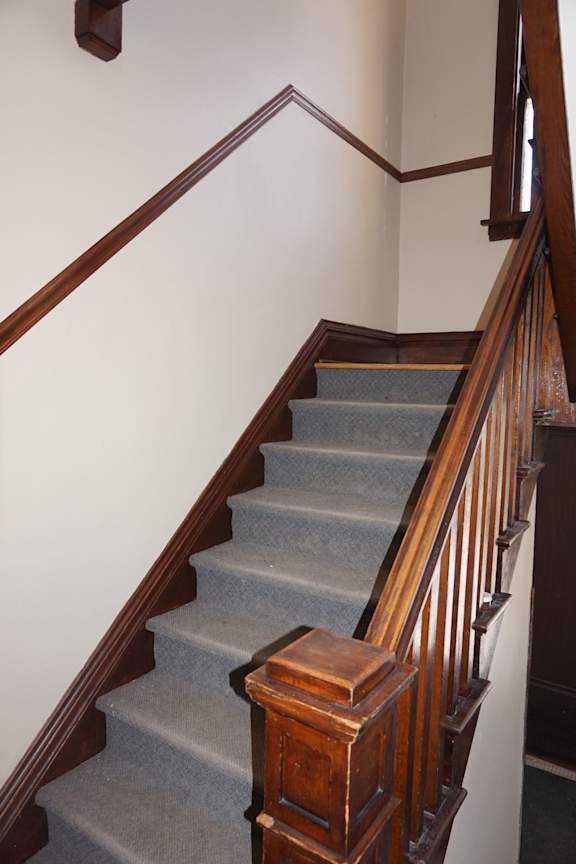 A staircase with a wooden handrail and a grey carpeted runner.