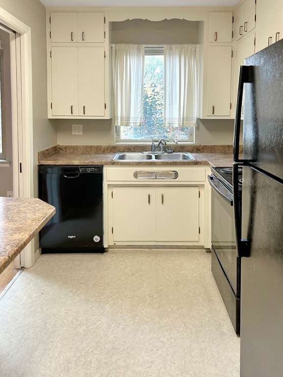 A black refrigerator sits in a kitchen with white cabinets.
