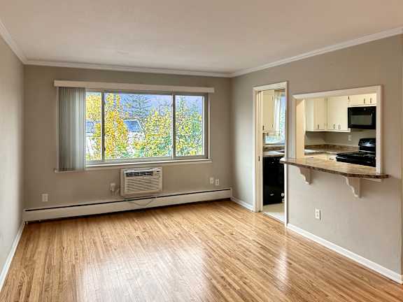 A room with a window, a microwave, and a wooden floor.