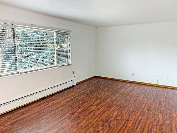 A room with a window covered in blinds and a wooden floor.