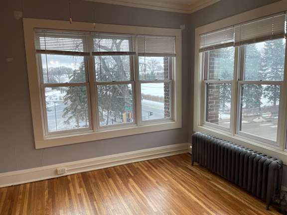 A room with a grey wall, a window with blinds, and a radiator on the floor.
