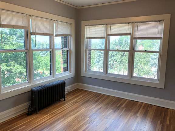 A room with wooden floors and two windows with blinds.