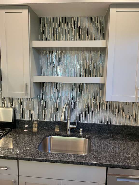 A kitchen with a sink and a backsplash made of silver tiles.