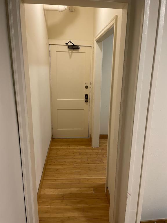 A white door with a black handle is in a hallway with wood floors.