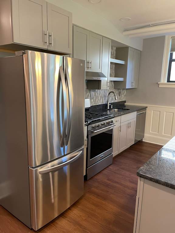 A stainless steel refrigerator in a kitchen with wooden floors.