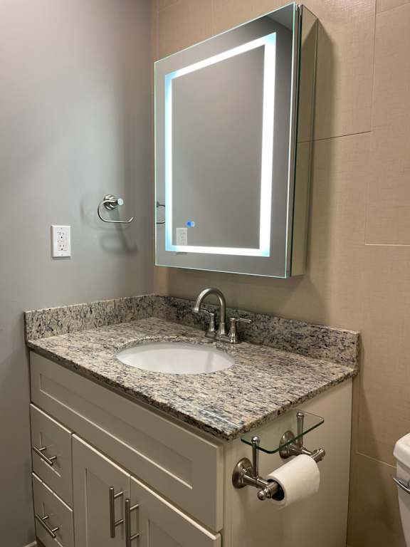 A bathroom with a sink, mirror, and toilet paper holder.